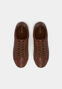 Brūni ādas sporta apavi ar gludu tekstūru, ar brūnām auklām, apaļu purngalu un baltu gumijas zoli. iekšējā oderē ir brūns audums.