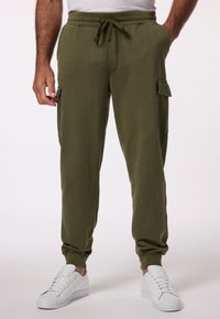 Olijfgroene cargobroek met een trekkoord in de taille, zijzakken en bijgesneden enkels, weergegeven met witte sneakers op een effen achtergrond.