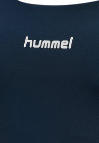 Hvid "hummel" logo trykt på en mørkeblå tekstureret stof baggrund, sandsynligvis en del af et beklædningsgenstand.