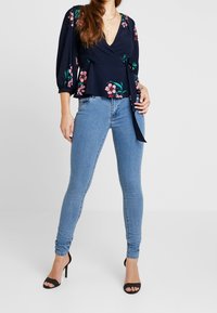 Navy blomsterwrap-top med puffede ærmer, parret med lyseblå skinny jeans. Sættet har højhælede sorte sandaler.
