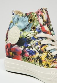 Hoge canvas sneaker heeft een kleurrijke bloemenprint, gouden oogjes, beige veters en een witte rubberen zool met een gestructureerd patroon.