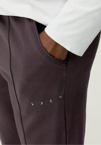 Mörklila mjukisbyxor med en sidficka och subtila fågelmönster i ljusgrått nära fickan. Mjuk tyg med en slät textur.