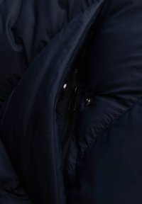 Granatowa kurtka puchowa z tkaniny o pikowanej strukturze, z widocznym zamkiem błyskawicznym z przodu i metalowymi zatrzaskami dla dodatkowego efektu.