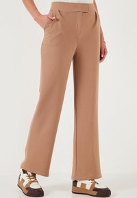 Beige, leveleggsbukser med strukturert overflate, frontfolder og sidelommer. Kombinert med flerfargede, klumpete joggesko.