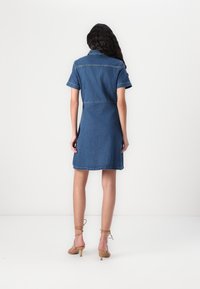 Vestido de ganga com mangas curtas, colarinho e bolsos traseiros. O tecido tem um tom de azul médio com costura em contraste.