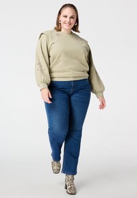 Lichtgroene sweater met pofmouwen en bloemenuitsnijdingen, gecombineerd met blauwe jeans en enkellaarsjes met slangenprint.