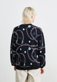 Suéter preto de malha com um padrão repetido de designs circulares em roxo e turquesa com acentos. Mangas longas e bainha canelada.