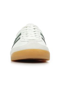 Scarpa sportiva bianca con strisce verdi, lacci e suola in gomma. Presenta una punta in suede e un materiale superiore liscio.