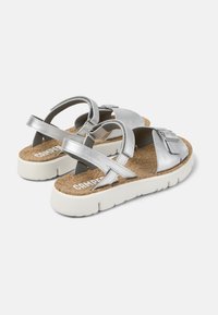 Silver metallic sandals with cork footbed, white thick sole, and crossed straps featuring adjustable buckles for a secure fit.