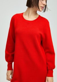 Rotes gestricktes Kleid mit rundem Ausschnitt, langen Ballonärmeln und gerippten Bündchen. Glatte Textur, lockere Passform, keine sichtbaren Muster oder Akzente.