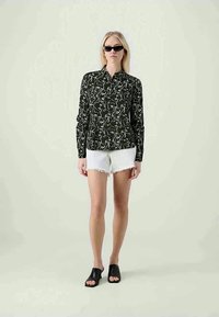 Μαύρο πουκάμισο με μακριά μανίκια και λευκό αφηρημένο σχέδιο, σε συνδυασμό με λευκά κοντά σορτς με φθαρμένα άκρα. Το μοντέλο φορά μαύρα γυαλιά ηλίου και ανοιχτά μαύρα σανδάλια.