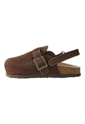 Brown suede clog with adjustable buckle strap, open heel, and cork footbed, designed for casual comfort and easy wear.