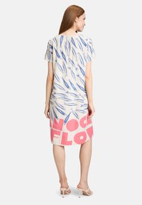 Leinenkleid mit einem blauen Fischmuster auf cremefarbenem Hintergrund, mit pinkem Text am Saum. Kurzärmliges und knielanges Design.