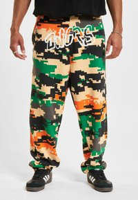 Farverige camouflage joggers i nuancerne grøn, sort, orange og beige. Løs pasform med en behagelig tekstur og grafisk skrift på fronten.