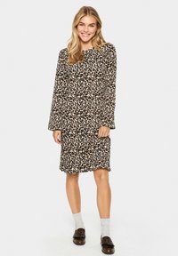 Leoprint-Kleid mit langen Ärmeln, rechteckiger Form, weichem Stoff und knielangem Design. Getragen mit grauen Socken und braunen Schuhen.