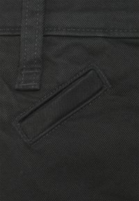 Denim nero con una superficie texturizzata, caratterizzato da una tasca a forma rettangolare con cuciture visibili e una finitura liscia.