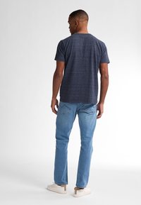 Tricou pentru bărbați de culoare albastru închis, cu dungi, cu mâneci scurte, purtat împreună cu blugi din denim deschis și adidași albi, văzut din spate.