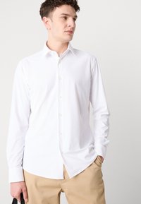 Hvit langermet skjorte med knapper og spiss krage, laget av glatt stoff; brukt sammen med kaki-bukser for en avslappet look.