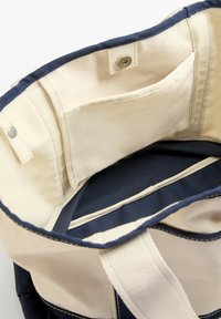 Platnena torba z bež notranjostjo in temno modrim obrobjem; ima žepe in zapiranje na klik; močni ročaji za nošenje.