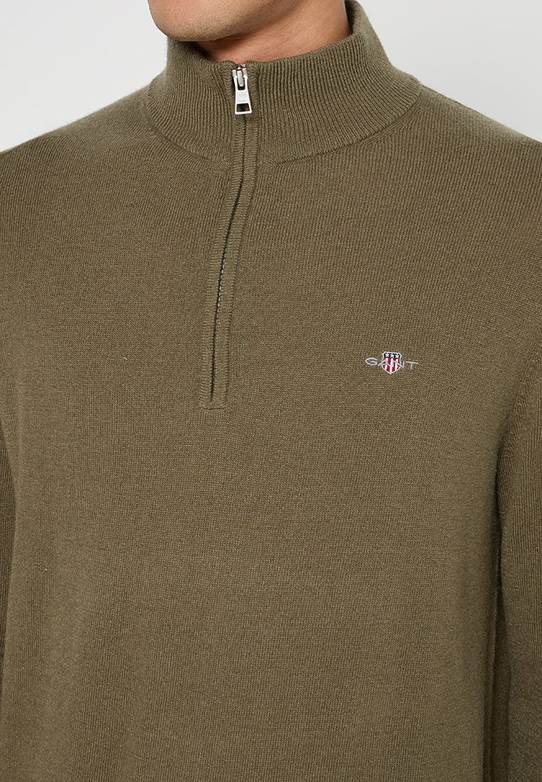 Olivnozielony, dziany sweter z rozpinanym zamkiem na ćwierć z prążkowanym kołnierzem i logo GANT. Posiada gładką fakturę i dopasowany krój.