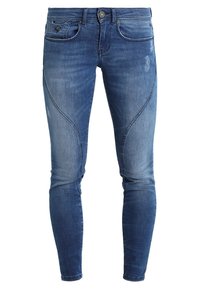 Modré džíny skinny s pěti kapsami, světlým vyblednutím a charakteristickými křivkami švů podél nohavic.