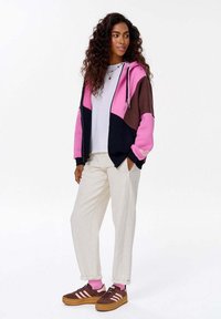 Bluza z kapturem w kolorowe blokady różowego, brązowego i czarnego; posiada zamek, sznurki oraz ściągacze. Połączona z białymi spodniami i brązowymi trampkami.