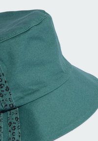 Zelený bavlnený klobúk v tvare vedra s textúrovaným povrchom a kontrastným čiernym vzorom zvierat po boku. Kruhový tvar koruny.