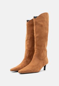 Καφέ καστόρινα μπότες μέχρι το γόνατο με μυτερό σχήμα, μικρό τακούνι και ραφές σε δυτικό στυλ μπροστά. Λεία υφή χωρίς διακοσμητικά.
