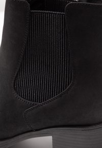 Botín negro con parte superior de ante, paneles laterales de elasticidad estriada y suela texturizada. El tacón es robusto y tiene forma de bloque.
