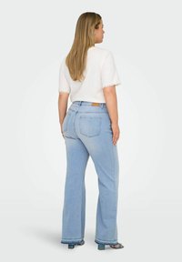 Lichtblauwe flared jeans met een middelhoge taille, vier zakken en een rafelig zoom. Gecombineerd met een witte top met kantafwerking op de mouwen.