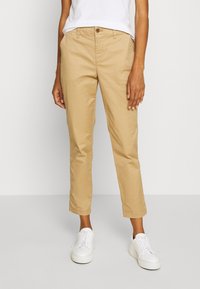 Chino cropped color khaki in cotone, con chiusura a bottone, tasche laterali e taglio dritto, abbinati a sneaker bianche.