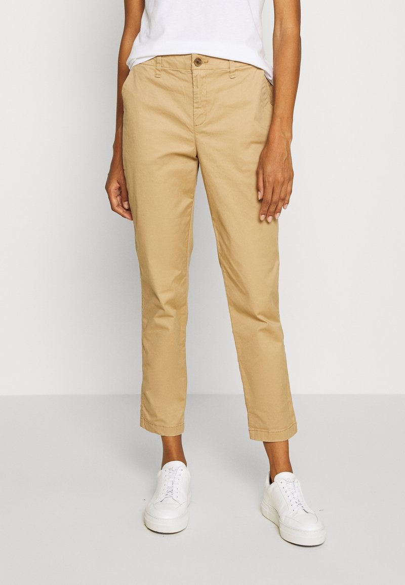 Chino cropped color khaki in cotone, con chiusura a bottone, tasche laterali e taglio dritto, abbinati a sneaker bianche.