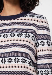 Pull avec un col côtelé bleu marine, un motif tricoté avec des bandes alternées en rose, blanc et noir, et des motifs de flocons de neige.