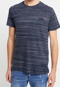 Tmavě modré tričko s krátkým rukávem a texturovaným pruhovaným vzorem. Obsahuje kulatý výstřih a malé logo v levém horním rohu.