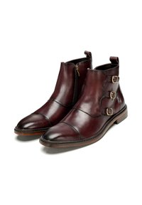 Botas de cuero burdeos hasta el tobillo con cremallera lateral, acentos de triple hebilla, diseño de punta recubierta y suela plana marrón. Textura suave en todo momento.