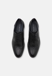Chaussures brogue en cuir noir avec des perforations détaillées, un design classique à lacets et une texture lisse et brillante.