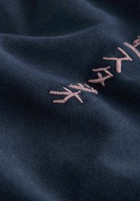 Nahaufnahme eines marineblauen Stoffs mit einer Reihe rosa bestickter Symbole oder Buchstaben auf der Oberfläche.