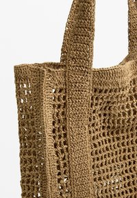Geflochtene Tragetasche aus naturfarbenem, strohähnlichem Material, mit einem offenen Netzdesign und zwei stabilen geflochtenen Hän-klen.