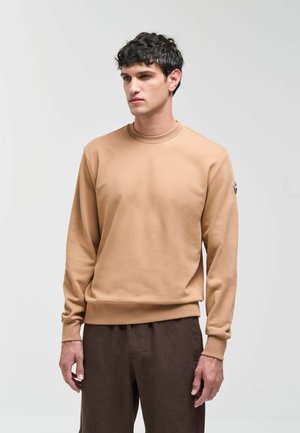 Beige sweatshirt gemaakt van zachte stof, met een ronde hals, lange mouwen en geribbelde manchetten. Gecombineerd met donkerbruine broek.