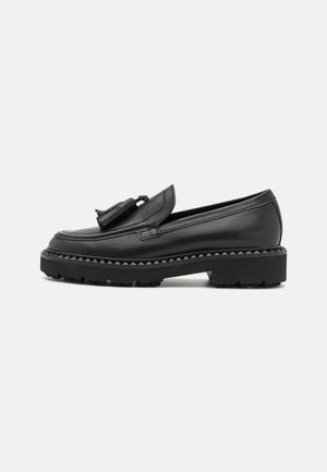 Mocassin en cuir noir avec un accent pompon, un bout arrondi et une semelle plateforme noire épaisse et robuste avec un bord dentelé.