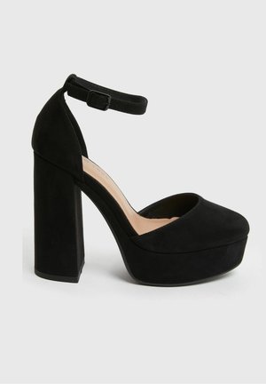 Černé semišové platformové lodičky s kulatou špičkou, silným blokovým podpatkem a páskem kolem kotníku. Mají hladkou texturu a měkkou podšívku.