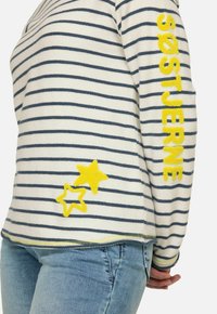 Maglione a righe in crema e navy con scritte gialle e ricami a stella sul davanti. Presenta una vestibilità rilassata e una texture morbida.