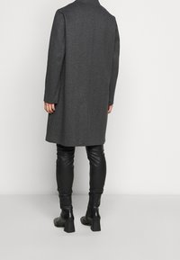 Šedý kabát ze směsi vlny s rybí kostí, s dlouhými rukávy a rovým střihem; kombinovaný s černými koženými legínami a kozačkami.