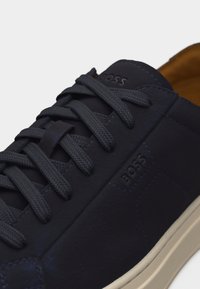 Δερμάτινο αθλητικό παπούτσι σε ναυτικό μπλε χρώμα με κορδόνια στο ίδιο χρώμα, ανάγλυλο λογότυπο BOSS στη γλώσσα και την πλευρά, και λαστιχένια σόλα σε εκρού απόχρωση.