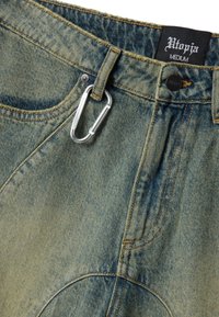 Denim jeans with a metal carabiner clipped to a belt loop and a black Utopia brand label showing size Medium on the waistband.