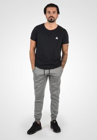 Sorte T-shirt med et trekantet logo, parret med lysegrå sweatpants. Outfittet har en afslappet pasform, og sorte sneakers fuldender looket.