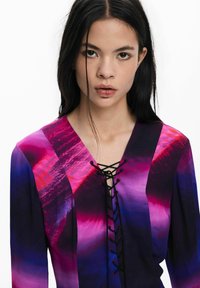 Pikendusega pluus, millel on pitsitud kaelus, elava lilla ja roosa gradiendi muster ning siidine tekstuur.