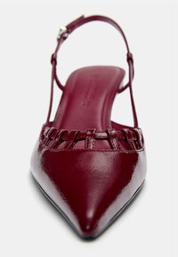 Chaussure pour femme à talon slingback, à bout pointu, de couleur rouge foncé brillant, avec de fines lanières horizontales à l'avant et une sangle à boucle à la cheville.