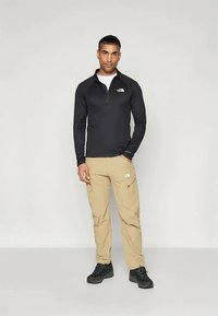 Čierny top s dlhým rukávom a štvrťovým zipsom a khaki cargo nohavice s zipsovými vreckami, doplnené o čierne turistické topánky. Minimalistický dizajn, ľahký materiál.