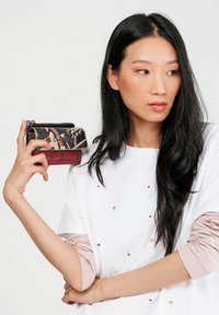 Portafoglio in una combinazione di nero e marrone, con motivi a scrittura e finitura texturizzata, dotato di una cerniera metallica e accenti rossi a contrasto.